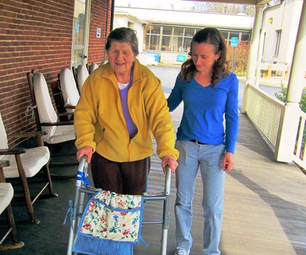 therapist helping elderly woman walk assisted