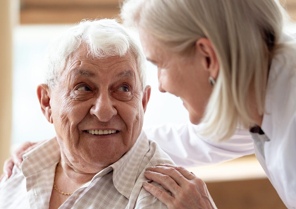 Head shot close up cheerful elderly man looking at pleasant middle aged nurse. Mature female doctor embracing shoulders, communicating with smiling 80s patient, giving support and psychological help.