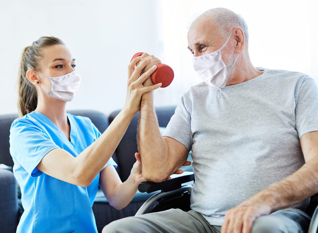 Doctor or nurse caregiver exercise with senior man, both wearing protective masks,  at home or nursing home