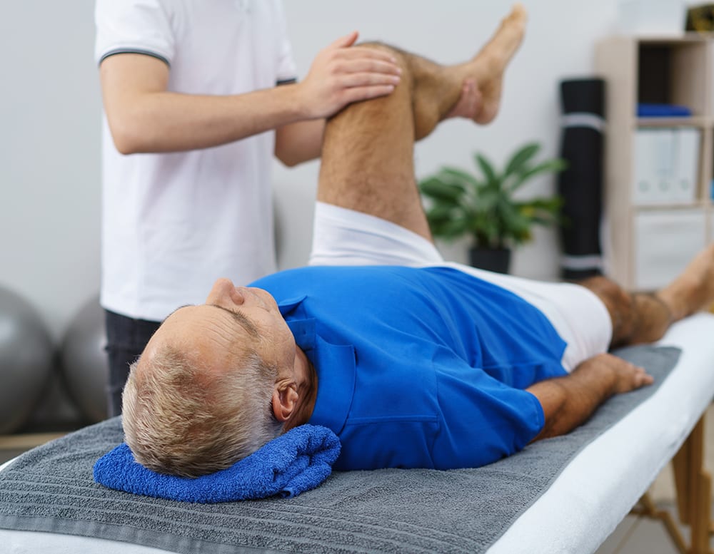 Physiotherapist working with an elderly patient doing mobility and functionality exercises with his left knee as he lies in an examination couch