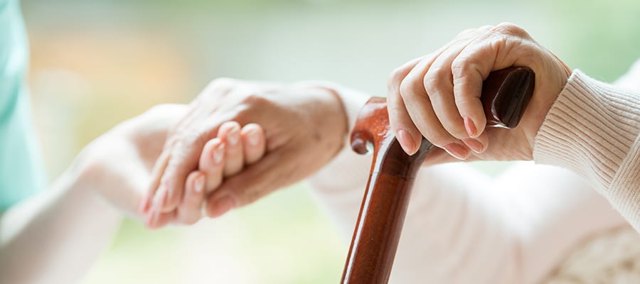 Elder person using wooden walking cane during rehabilitation in friendly hospital